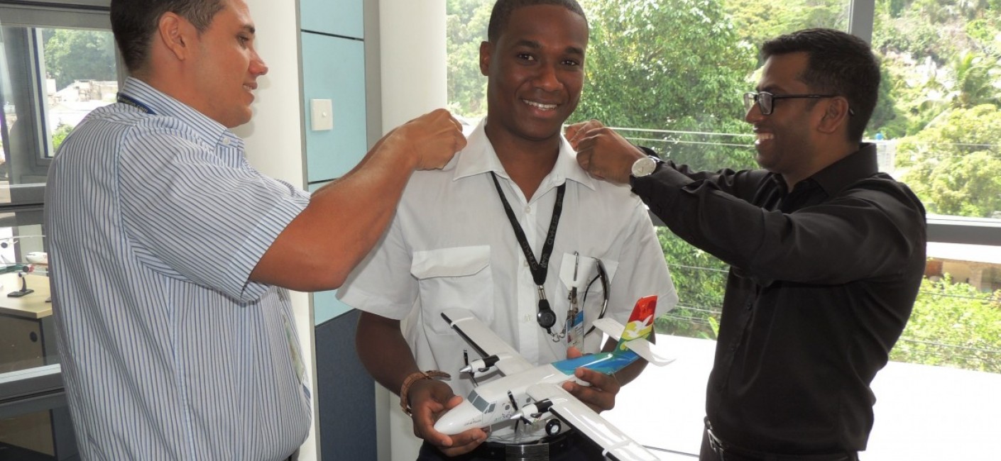Captain Sandy Benoiton, Head of Crew Training (left) and Manoj Papa, Air Seychelles’ Chief Executive Officer (right), fasten Captain Morel’s epaulettes as he holds a model of the Twin Otter aircraft he now commands